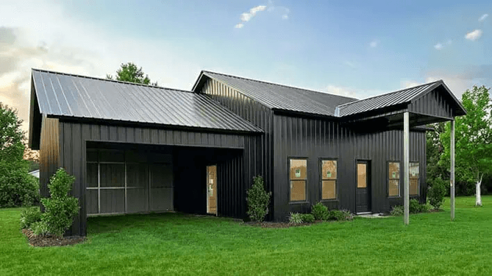 Modern all-black barndominium with dual-peak vertical roof, open framed side bay, and covered porch — Get Carports